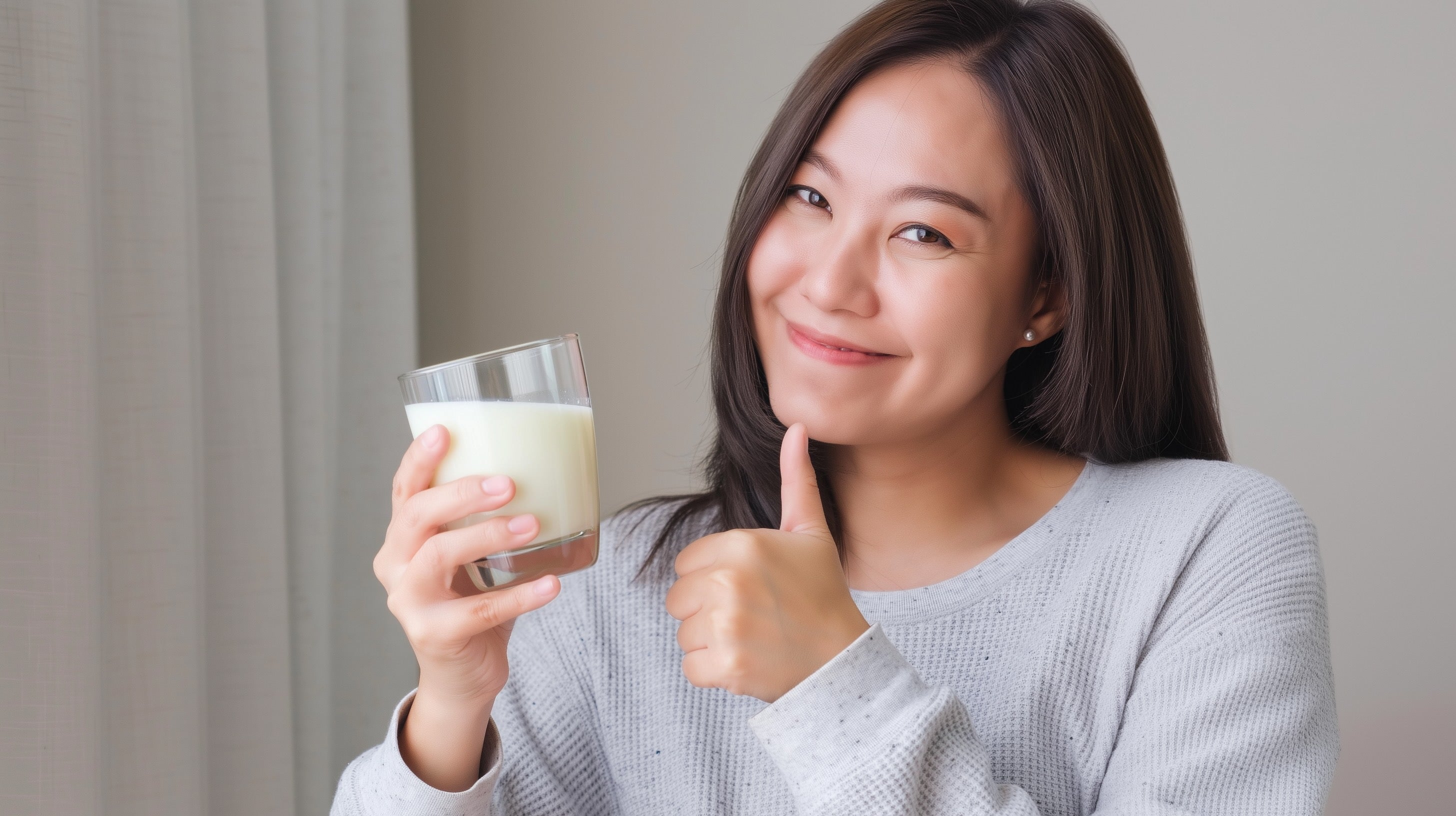 Woman smiling and giving thumbs up while holding a glass of oat milk