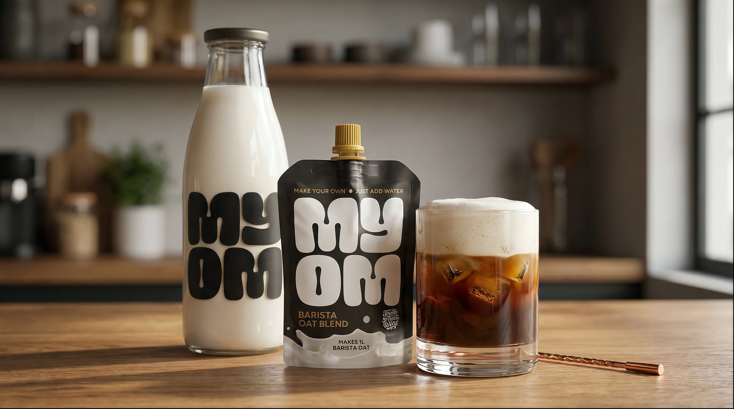 MYOM Barista Oat cold foam crowning a double-shot iced long black in a tall glass, set on a kitchen counter.