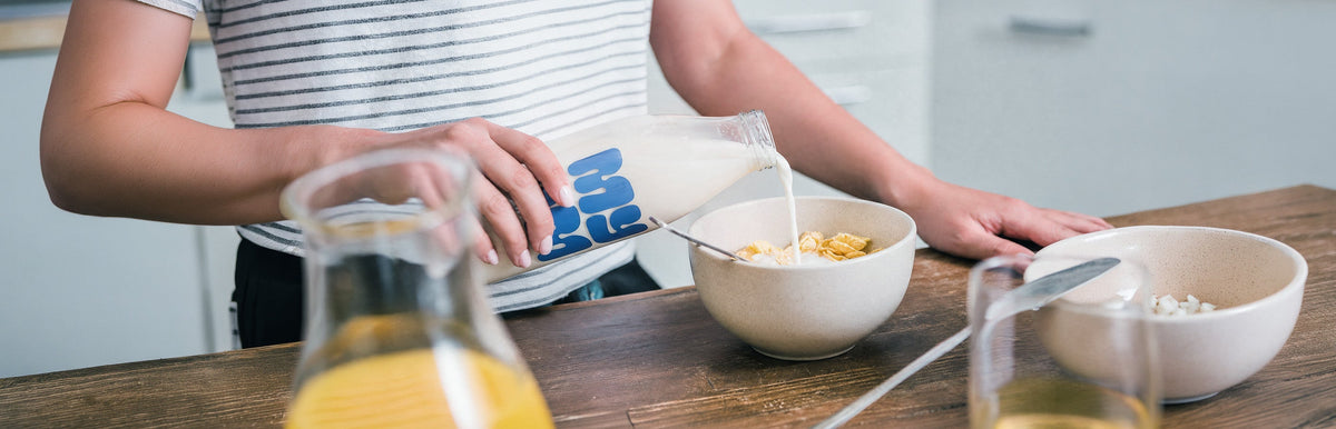 MYOM oat drink being poured from a glass bottle into a bowl of breakfast cereal.
