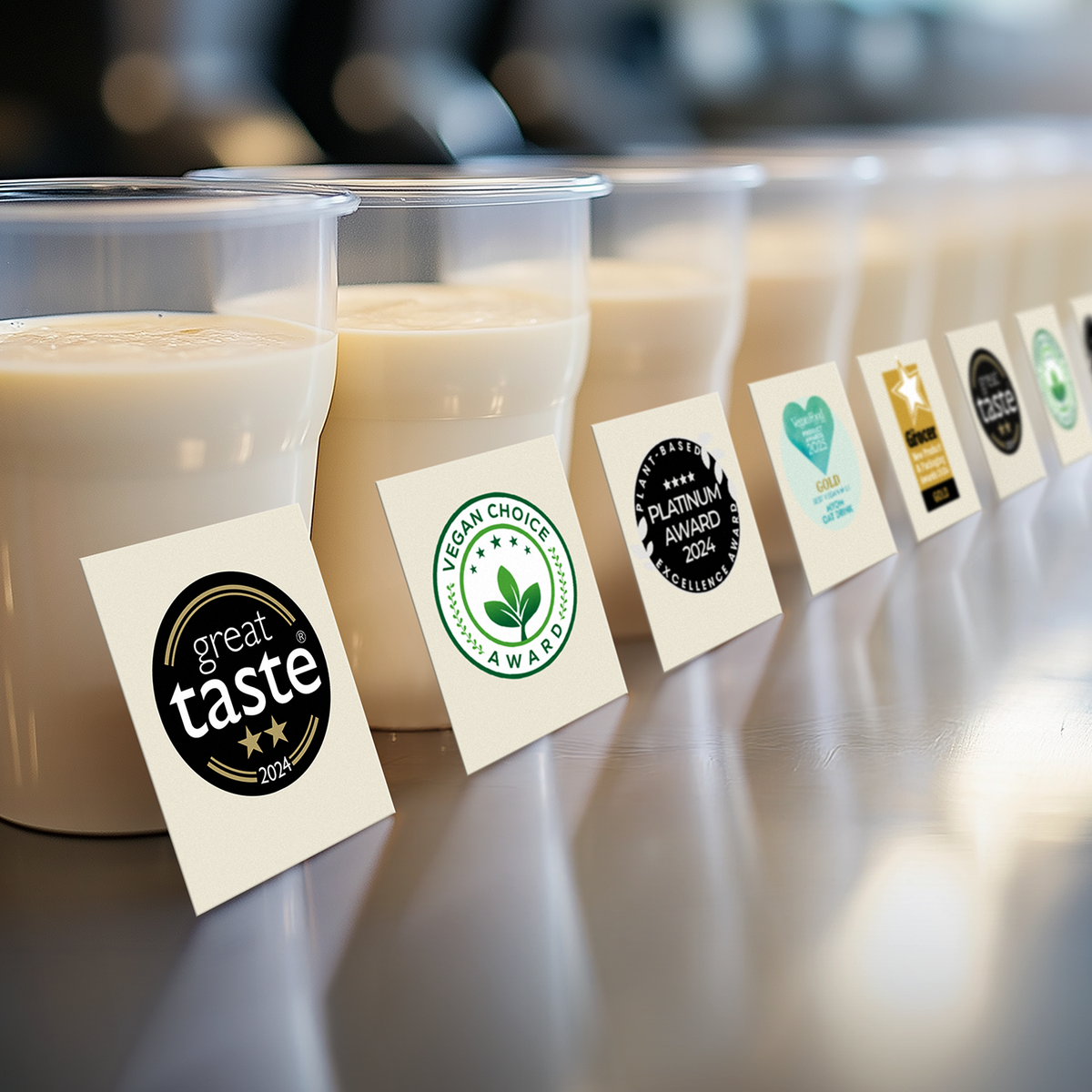 MYOM Original Oat and MYOM Barista Oat pouches with their award badges: Vegan Food & Living Product Awards, Great Taste 2-star, Great British Food Awards, The Grocer New Product & Packaging Awards and Plant-Based Excellence Awards Platinum