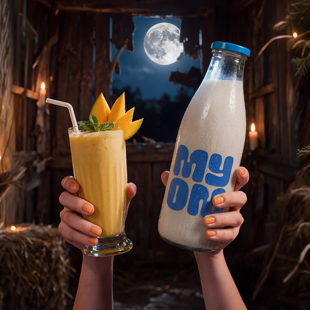 Golden MYOM Mango Mayhem with a mango garnish beside a MYOM glass bottle in a candlelit Halloween setting.