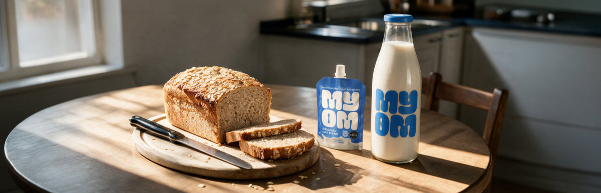 Oat-topped porridge bread loaf and slices on a wooden board beside a MYOM Original Oat Drink Premix pouch and a bottle of oat drink.
