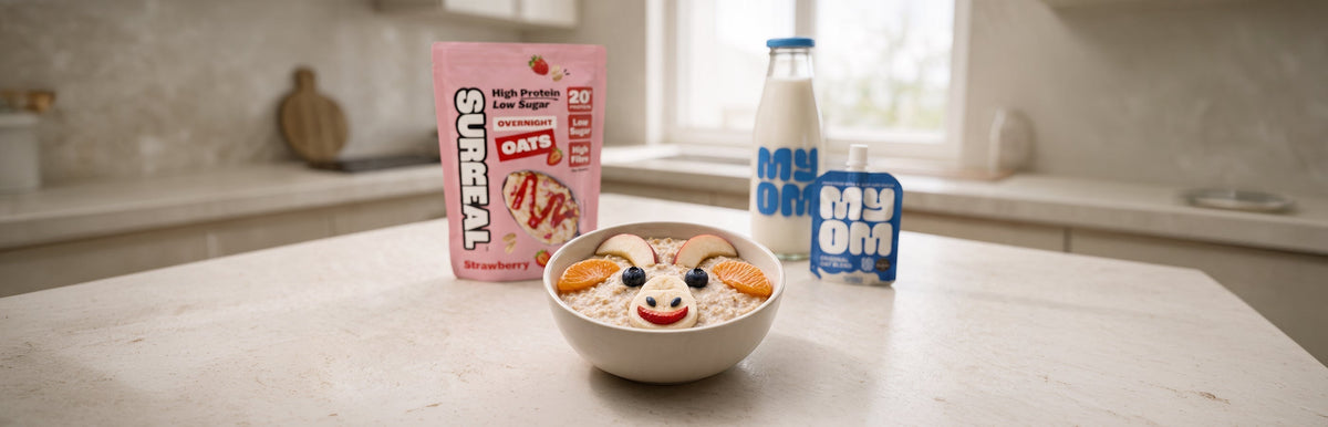 Strawberry overnight oats decorated as a goat face with apple horns, satsuma ears, blueberry eyes, a banana muzzle and strawberry smile, beside SURREAL and MYOM packs for World Porridge Day 2026.