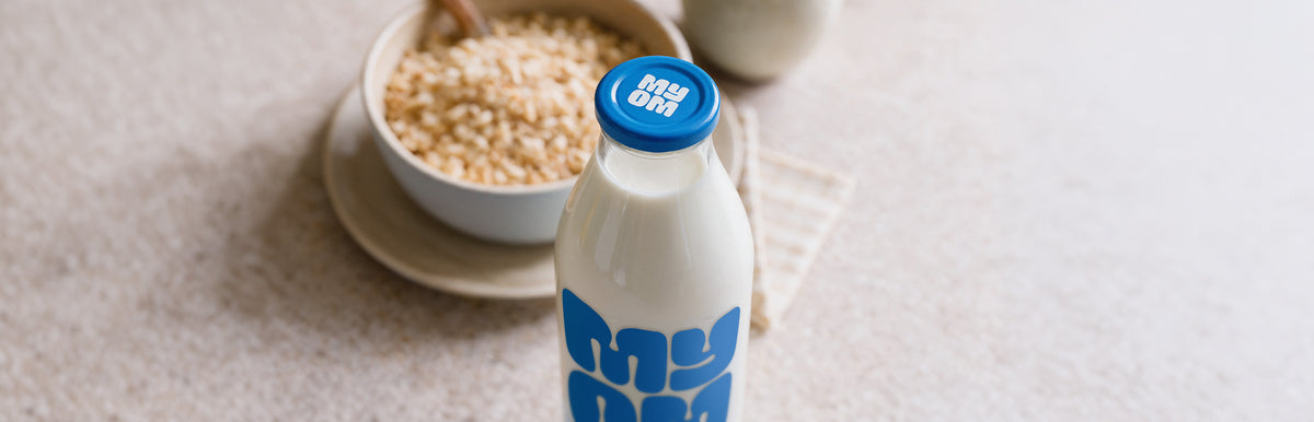 A MYOM oat drink bottle beside a bowl of cereal on a kitchen counter.