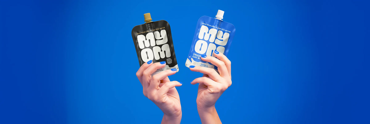 MYOM Original oat milk premix and MYOM Barista oat milk premix pouches held side by side against the brand blue