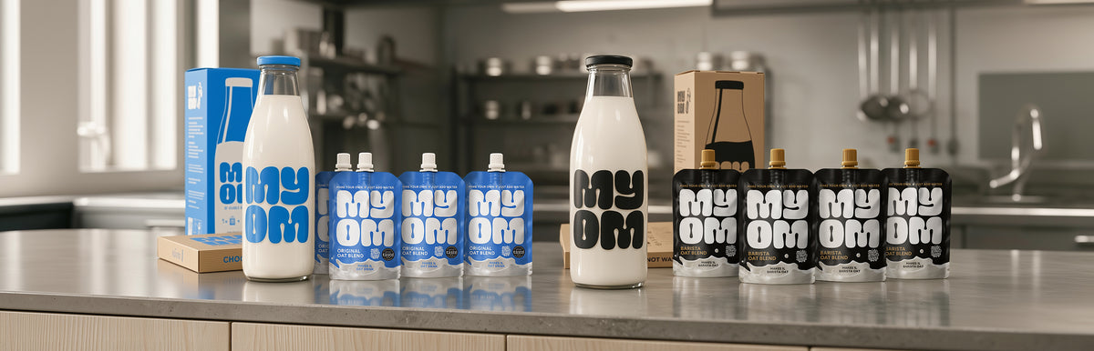 MYOM Original and MYOM Barista oat milk premix pouches, 1L glass bottles and letterbox boxes together on one kitchen counter
